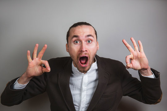 Excited businessman gesturing OK and screaming on gray