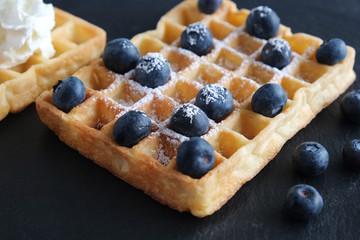 Fresh Belgian or Viennese waffles with blueberries closeup on a black background Dessert for breakfast.