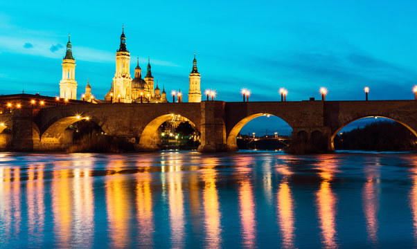 Basilica del Pilar and Puente de Piedra reflected in the Ebro river during the blue hour in Zaragoza, Spain
