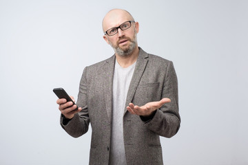 Mature frowning disgusted man surfing smartphone in dislike. His payment is declined. Studio shot