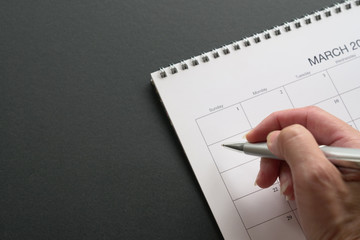 White clean calendar on black or grey background with copy space. Hand holding a pen. Business meeting and schedule concept.