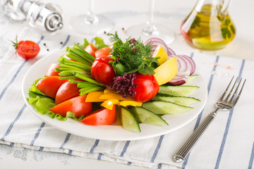 Assorted fresh vegetables on a plate. Tomatoes, cucumbers, onions, peppers, herbs.