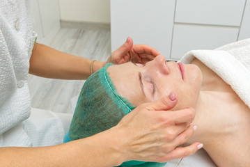Beautician applies a natural moisturizing mask to the face of a young beautiful woman. Anti-aging...