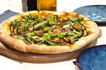 Italian pizza with bacon and arugula, balsamic vinegar, olive oil, blue plates in restaurant