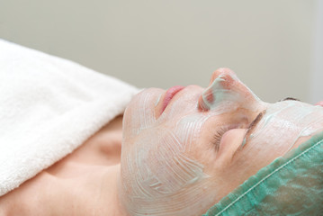 Naklejka premium beautiful young woman with natural moisturizing mask on the face. Beauty treatment. Anti-aging skin and facial wrinkles. Cosmetology concept. The cosmetologist performs the procedure to cleanse the
