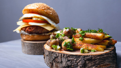 fried potatoes with mushrooms and a juicy burger on forest wooden boards..home fast food.