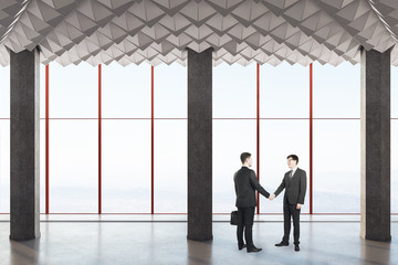 Fototapeta premium Business people shake hands in modern concrete interio