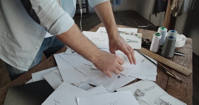 Close-up shot of hands of a clothes designer touching different beutiful sketches of new clothing collection - small business, art concept 4k footage