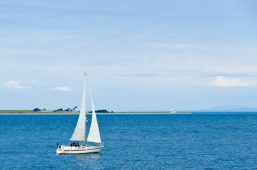 Naklejka premium Nice cruise yacht in the ocean over a lighthouse and blue sky.