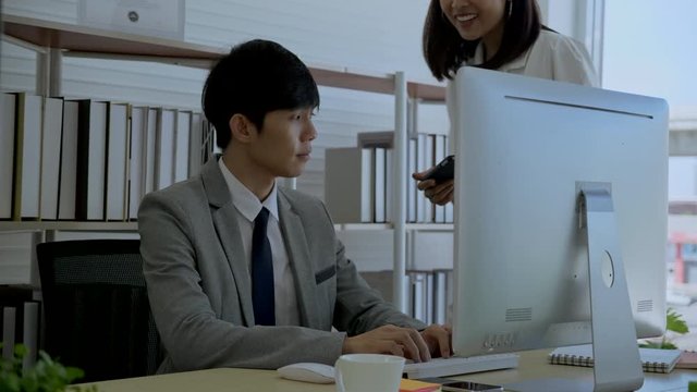 Asian businessmen sit and work using computer in the office and Woman staff comes to sign the agreement documents on the tablet. Working system marketing plan And business cooperation