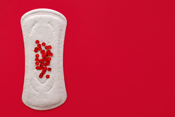Menstrual pad with red sequins on a red background, top view, miniature of the menstrual period