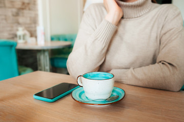 Business negotiations and business lunch in a cozy cafe. Coworking, working outside the home. A black phone with a mint-colored case and a blue-and-white mug on the background of a man without a face.