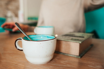 Beautiful porcelain small mug white outside blue inside on a wooden table in a cafe on the background of a thick book. A cozy Breakfast in a bright restaurant.