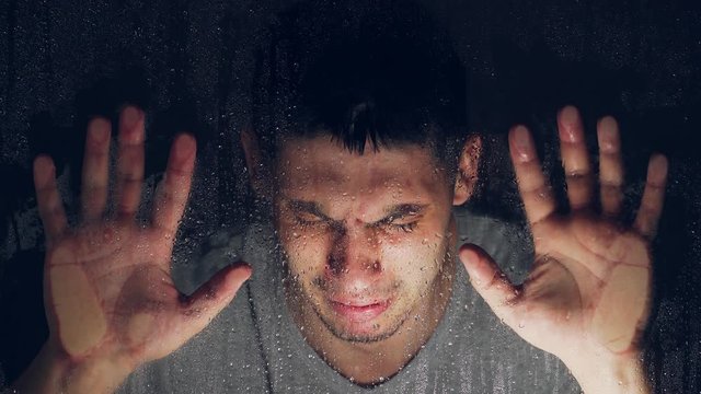 The theme of depression and loneliness. Caucasian Boy crying behind clear glass in a drop of water. On a dark background. Close-up