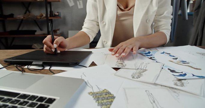 An unrecognizable tailor is working at her office, drawing sketches from paper to graphics tablet, working on her new collection - fashion concept 4k footage close up