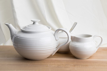 a white ceramic teapot sugar and cream set on a wooden table top