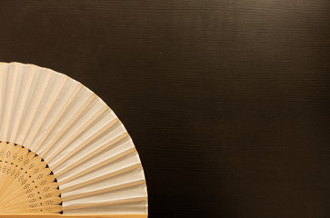 Hand fan, or folding fan, on dark brown copy space background. 
