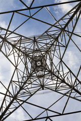 Steel lattice structure of a high voltage electricity pylon creates a geometric pattern against a blue sky with clouds.