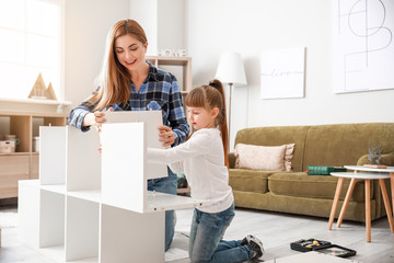 Mother and her little daughter assembling furniture at home