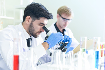 Team of scientist research working together conduct experiments and looks on  microscope in modern laboratory / Scientists in lab biochemistry genetics forensics microbiology and test tube