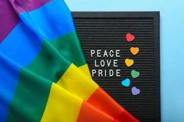 Board with words PEACE, LOVE, PRIDE and rainbow flag on color background. LGBT concept