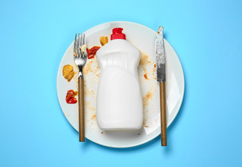 Dirty empty plate with cutlery and detergent on color background