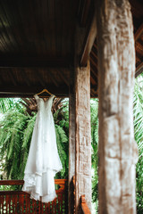 White wedding dress hanging on terrace of wooden rustic house in garden