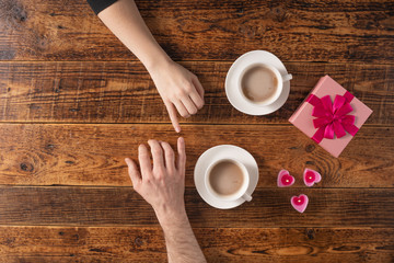 Valentine's Day celebration concept. A nice gift for your loved one. Hands of man and woman with coffee mugs on a wooden table background. Copy space. Flat lay. Close-up.