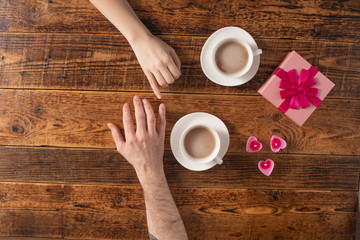 Fototapeta na wymiar Valentine's Day celebration concept. A nice gift for your loved one. Hands of man and woman with coffee mugs on a wooden table background. Copy space. Flat lay. Close-up.