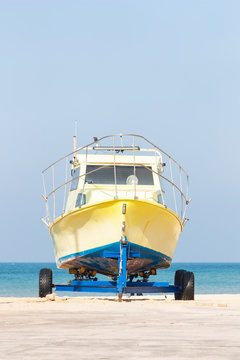 a yellow boat stands on a trailer on a sandy beach