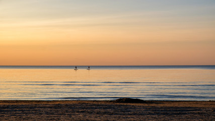 Fototapeta na wymiar Sunset on the sea coast. Two rowers on the boards, sandy beach. Water sports.