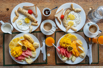 Tropical breakfast of fruit, coffee and scrambled eggs and banana pancake for two on the beach near sea. Top view, table setting.