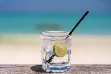 Soda water with lime and ice on a wooden table near the sea on the beach
