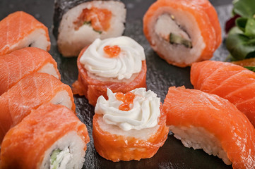 Close-up sushi and rolls with salmon and salad on a black flat tuff plate. Tasty oriental food