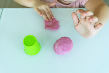 little girl sculpts a pyramid of pink plasticine in the kitchen. children's creativity and development