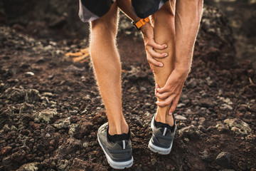Male runner holding injured calf muscle and suffering with pain. Sprain ligament while running outdoors. View from the back close-up. - obrazy, fototapety, plakaty