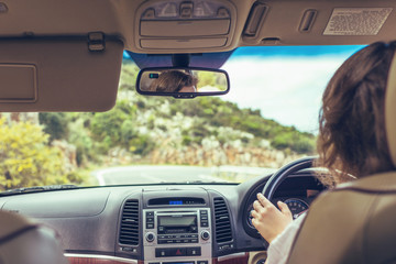 Woman driving a car relaxing in auto trip traveling along ocean tropical beach in background. Traveler concept. Back view