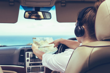 Woman driver in the headphones driving a car and looking at th map. Girl relaxing in auto trip...