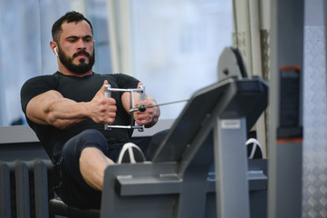 Fototapeta na wymiar fitness training in sport gym of young active caucasian male with beard sitting and pulling heavy weight on exercise equipment listening music for motivation wearing headphones