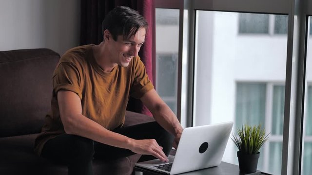 Happy young man using laptop computer for ecommerce doing online shopping watching video movie sitting on sofa at home