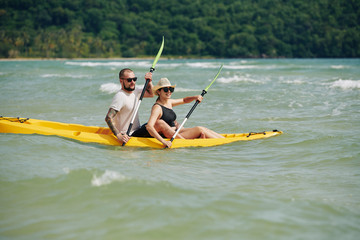 Adventerous excited young couple in sunglasses kayaking on lake