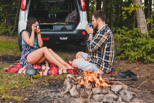 couple sitting on blanket near bonfire white suv vehicle on background