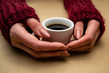 Hands in a sweater hug a cup of coffee on a beige background