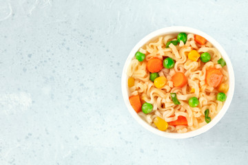Ramen cup, instant soba noodles in a plastic cup, with green peas, carrot pieces, and scallions, top-down shot with copyspace
