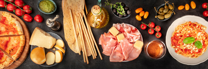 Italian food panorama. Pizza, pasta, cheese, ham, capers, wine, tomatoes, shot from the top on a black background