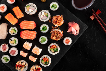 Large sushi set with soy sauce and chopsticks, top shot on a black background with copy space. A flat lay of various maki, nigiri and rolls