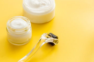 Dermaroller for home cosmetologic procedure near creams on yellow background copy space