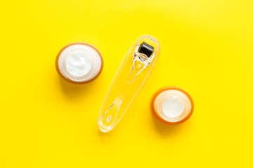 Dermaroller for mesotherapy near creams on yellow background top-down flat lay
