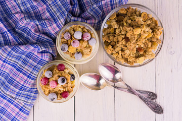 Two jars of fresh yogurt with frozen berries and granola on a white wooden table. Flat lay.