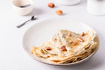 Crepes with poppy seed served with honey and pecans on grey background. Pancake week, mardi gras, maslenitsa holidays. Selective focus